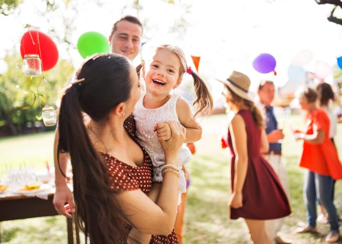 Family celebration outside in the backyard. Big garden party or birthday party. Young mother holding a small girl.