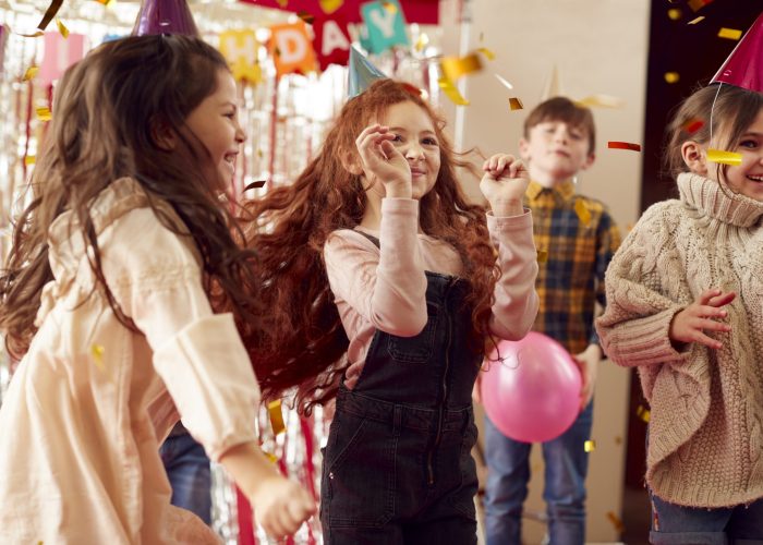 Group Of Children Dancing As They Celebrate At Birthday Party With Paper Hats